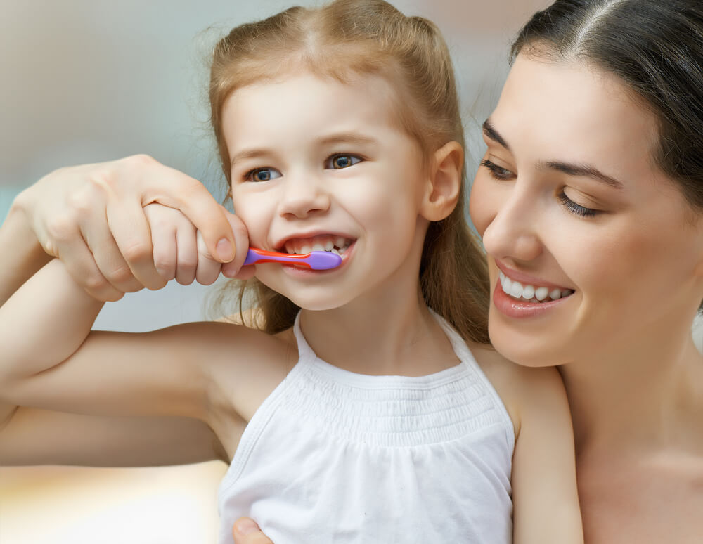 Mother teaching her daughter to brush her teeth